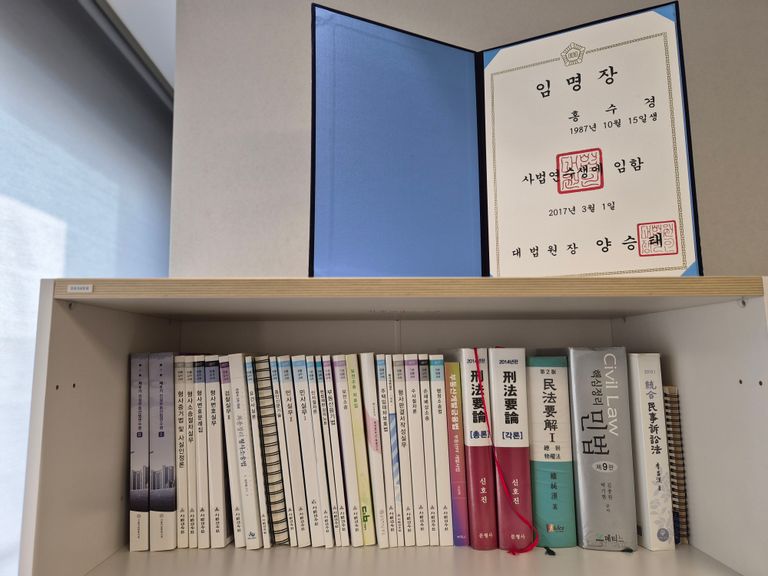 홍수경 변호사의 책상 한편에 놓인 사법연수생 임명장과 법률 서적들. "전문성은 탄탄한 기본기에서 나온다"는 신념을 지키기 위해, 그는 변호사가 된 지금도 사법시험 시절 보던 손때 묻은 기본서와 연수원 교재를 가까이 두고 끊임없이 연구한다. /홍수경 변호사